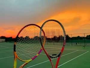 Permainan tenis di lapangan luar ruangan dengan net panjang dan raket besar