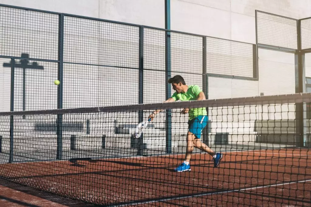 Pemain padel bertahan dengan tenang menghadapi lawan agresif yang melakukan smash keras di lapangan padel